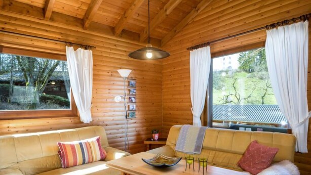 A cozy cabin interior with wooden walls, a sofa, a table with a bowl and glasses, and a window with curtains. - Reinskopf by Interhome (Schönecken)
