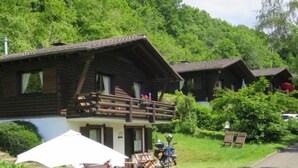 A wooden cabin with a balcony, surrounded by lush greenery and a clear sky. - Reinskopf by Interhome (Schönecken)