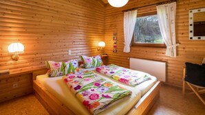 A wooden cabin bedroom with a double bed, two bedside lamps, a window with curtains, and a wooden ceiling. - Reinskopf by Interhome (Schönecken)
