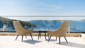 Un balcón con sillas de mimbre y una pequeña mesa, con vistas a un paisaje costero.
