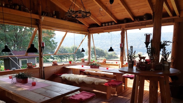 A wooden cabin with a large window, wooden benches, a table, and various potted plants. - In the middle of nature -Lavender hut- 9m² for 1-2 persons at Hilkenberg (Bodenfelde)