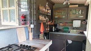 A compact kitchen with a gas stove, wooden utensils, a kettle, and various food items on shelves. - In the middle of nature -Lavender hut- 9m² for 1-2 persons at Hilkenberg (Bodenfelde)
