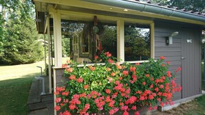 Ein kleines, eingeschossiges Gebäude mit einer Veranda und einem Blumenkasten mit roten Blüten.