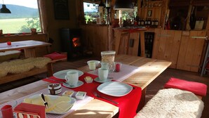 Ein Holztisch ist gedeckt mit Tellern, Tassen und Besteck, bedeckt mit einer roten Tischdecke und einem Fell.