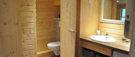 Een houten badkamer in een vakantiehuisje, met toilet, wastafel en een spiegel boven de wastafel.