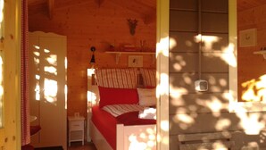 Ein gemütliches Blockhauskabinenzimmer mit Bett, Nachttisch, kleinem Tisch und einer Wandregal.