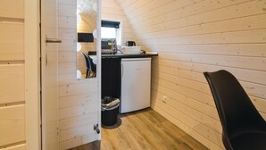 Een kleine keuken met houten wanden, een witte koelkast, een wastafel en een zwarte stoel.