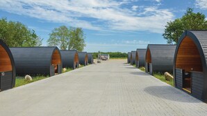 Een rij moderne, gebogen cabins met houten lambrisering en een verharde looppad die naar een centraal punt leidt.