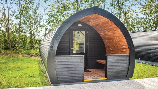 Een kleine, halvemaanvormige houten constructie met een deur en een bankje ervoor.