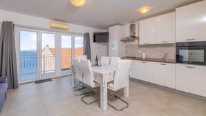Una cocina moderna con armarios blancos, una mesa de comedor con sillas, un horno empotrado y vistas al mar a través de amplias ventanas.