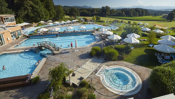 A large outdoor swimming pool with multiple lanes, surrounded by lounge chairs and umbrellas, set against a backdrop of trees and distant mountains. - Ferienwohnung "Meine Kleine Auszeit", 50 qm, Dachgeschoss, 1separates Schlafzimmer (Höslwang)
