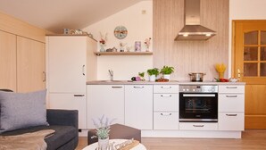 A modern kitchen with white cabinets, a built-in oven, and a wooden countertop. - Ferienwohnung "Meine Kleine Auszeit", 50 qm, Dachgeschoss, 1separates Schlafzimmer (Höslwang)