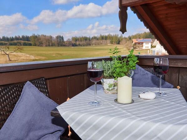 A balcony with a table set for two, featuring two wine glasses, a candle, and a potted plant.