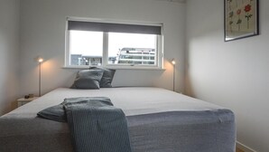 Une chambre à coucher avec un lit, une fenêtre, deux lampes de chevet et une œuvre d’art florale encadrée accrochée au mur.