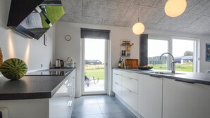 Une cuisine moderne dotée d’un grand îlot central, d’un four encastré et offrant une vue sur l’extérieur.