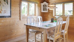 L’intérieur d’un chalet en bois, avec une table à manger, des chaises blanches et un meuble de rangement au-dessus de la table.