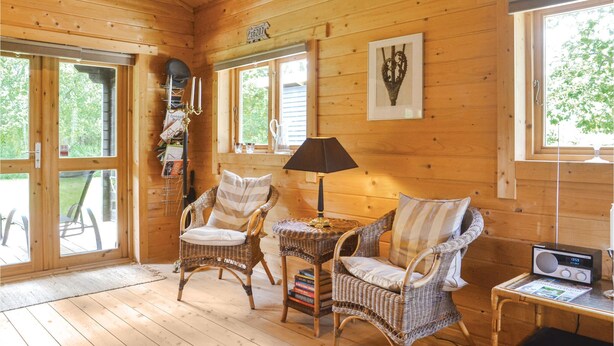Une pièce chaleureuse aux murs et au plancher en bois, avec des fauteuils en osier, une petite table avec une lampe et une radio.