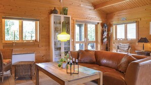 L’intérieur chaleureux d’un chalet avec un plancher en bois, un canapé en cuir marron, une table basse en bois, des chaises en osier et un meuble avec des portes en verre.