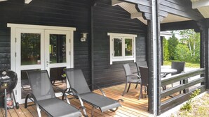 Un espace extérieur abrité comprenant deux chaises longues et une table, un barbecue, ainsi qu’une fenêtre donnant sur la verdure.
