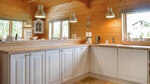 Une cuisine avec des meubles blancs, un plan de travail en bois, des luminaires suspendus et une fenêtre donnant sur un paysage verdoyant.