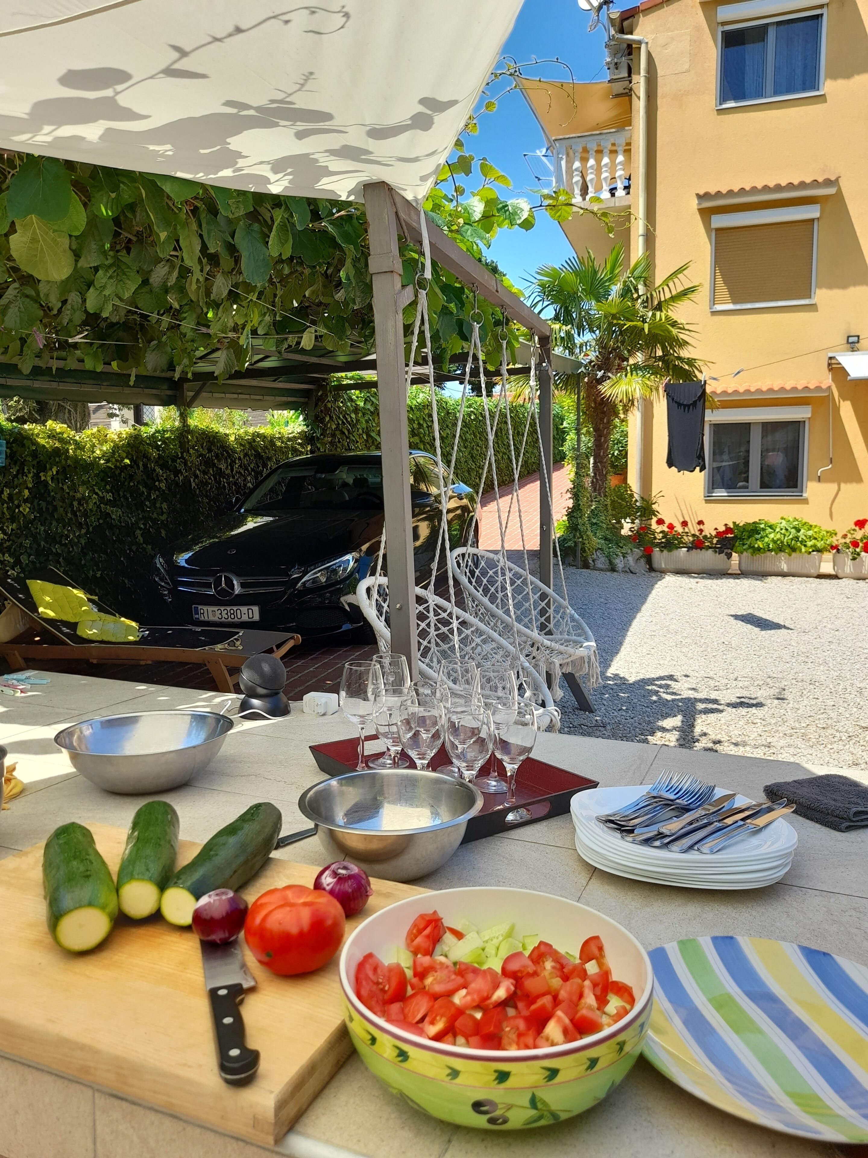 An outdoor dining setup with a table, bowls, cut vegetables, and a car in the background.