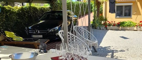 Mobiliario de comedor al aire libre con una mesa, cuencos, verduras cortadas y un coche al fondo.