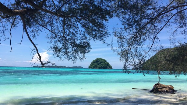 A beach with clear turquoise water, a sandy shore, and a small island in the distance. - GreenHouse EcoLodge (Kampung Mantanani)