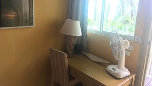 A room with a desk, a chair, a standing fan, a lamp, and a window with curtains. - GreenHouse EcoLodge (Kampung Mantanani)