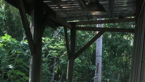 An outdoor wooden deck with two white chairs and a table, surrounded by lush greenery. - GreenHouse EcoLodge (Kampung Mantanani)