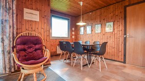 En inredning med träpanel, ett matbord, stolar, en gungstol av rotting och ett fönster.