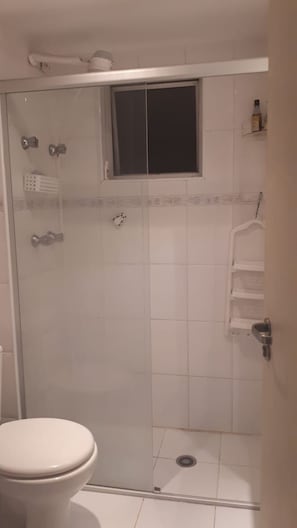 Cabina de ducha con puerta de cristal, inodoro y una pequeña ventana sobre la ducha.