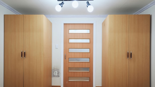 Une chambre avec deux lits, une armoire en bois dotée d’une porte au design original et un luminaire fixé au plafond.