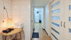 Un couloir avec un fauteuil en osier, une pile de serviettes et une lampe.
