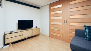 Une chambre moderne avec une armoire en bois, un téléviseur posé sur un meuble en bois et un canapé gris.
