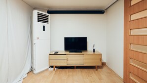 Une petite pièce, de taille modeste, comprenant un meuble en bois, un téléviseur à écran plat et un climatiseur fixé au mur.