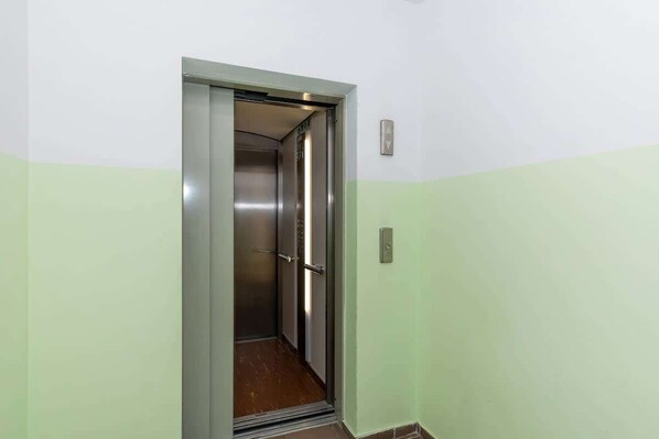 Un ascensor con interior metálico y pared verde.