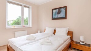 Un dormitorio con dos camas, una ventana, un radiador, una mesita de noche y un cuadro en la pared.