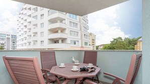 Un balcón con una mesa redonda y cuatro sillas, una gaviota y un edificio al fondo.