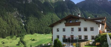 A two-story building with a balcony, surrounded by a well-maintained lawn and a mountain backdrop.