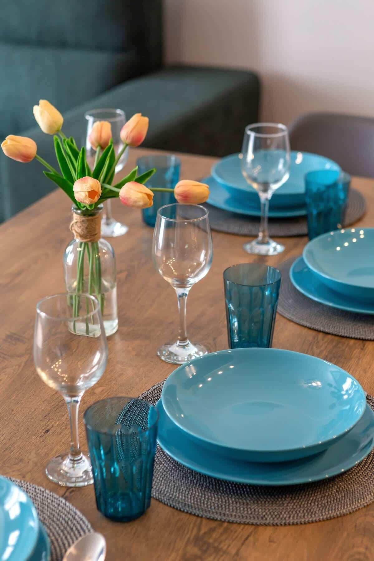 Ein Esstisch mit blauem Geschirr, Gläsern und einer Vase mit Tulpen.