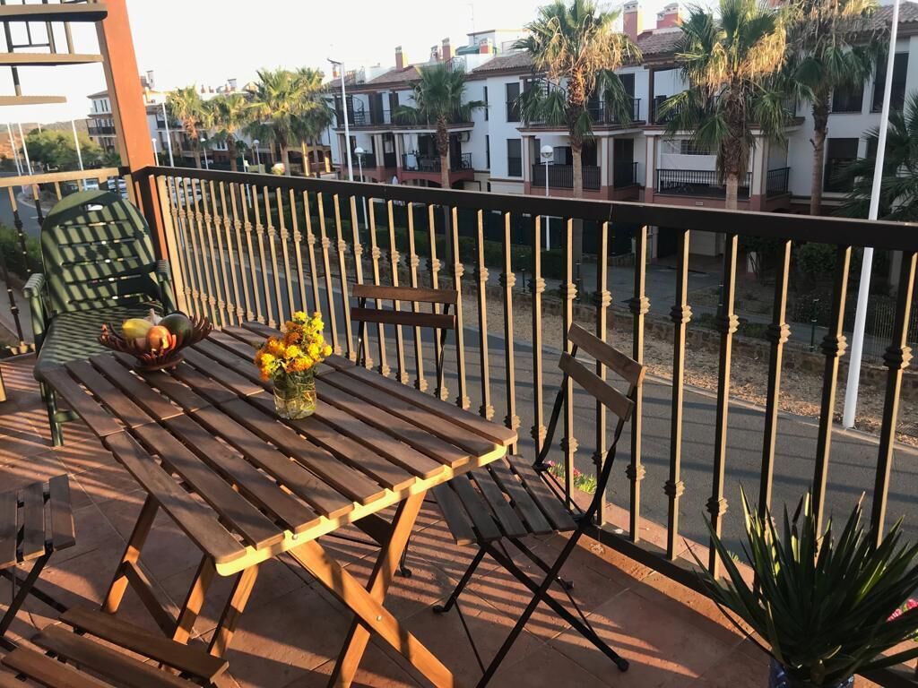A wooden deck with a table and chairs, a vase with flowers, and a railing.