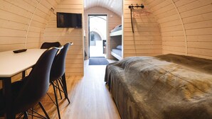 A compact room with a bunk bed, a table with chairs, and a television mounted on the wall.