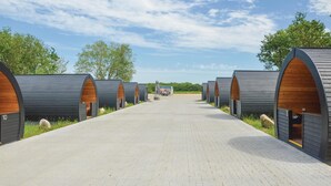 A row of modern, arched, wooden pod-style accommodations with a paved walkway leading to a truck in the distance.