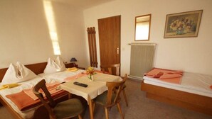 Una stanza con un letto, un tavolo con sedie, un termosifone e una porta.