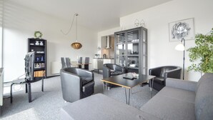 Una sala de estar moderna con un sofá gris, dos sillas de cuero negro, una mesa de centro de madera, un mueble de TV negro, un armario gris y una lámpara colgante.