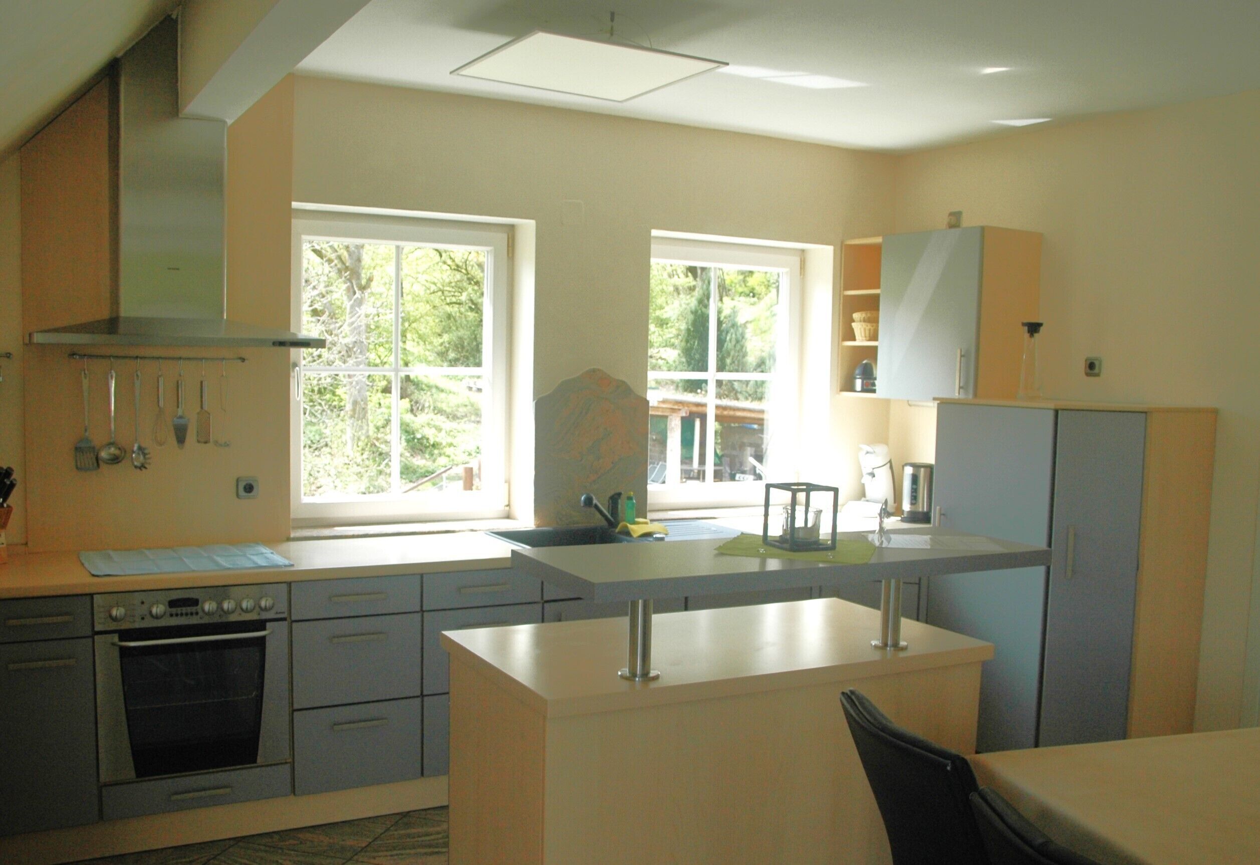 A kitchen with a stove, oven, sink, and cabinets. There are windows providing natural light and a view of greenery outside.