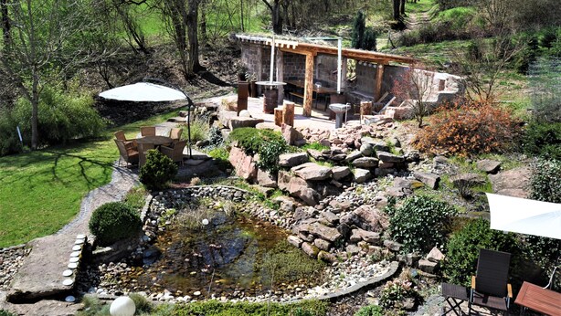 A garden with a pond, stone seating, and a wooden pergola. - Vacation home/event location, 285 m² living area, 300 m² secluded outdoor area  (Rieneck)