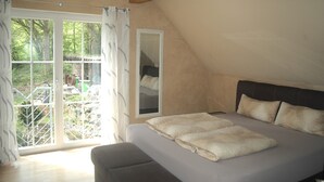 A bedroom with a large bed, a view of a garden through a sliding glass door, and a mirror on the wall. - Vacation home/event location, 285 m² living area, 300 m² secluded outdoor area  (Rieneck)