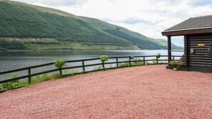 A wooden cabin with a gravel path leading to a wooden fence overlooking a lake and hills. - Vacation home Birch by Interhome (Invergarry)