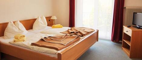 Une chambre d’hôtel avec un lit, une télévision, un bureau et une fenêtre avec des rideaux.